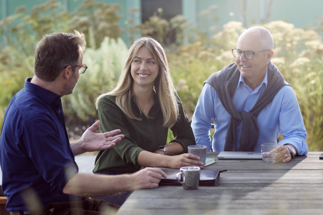 Three people sitting outside by a table.