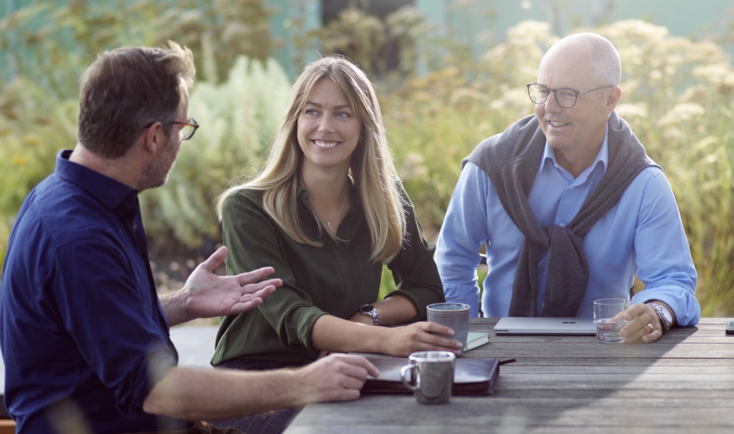 Three people sitting outside by a table.