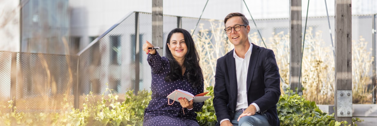 Two people sitting on a bench on a roof terrace.