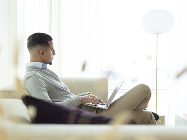 A person sitting in a sofa with a laptop.