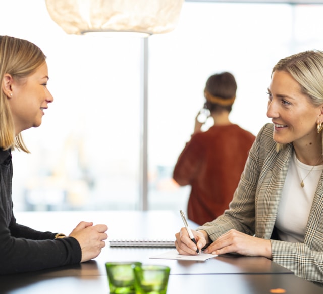 Two people talking to each other sitting by a table.