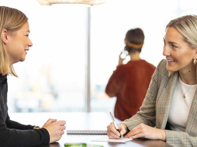 Two people talking to each other sitting by a table.