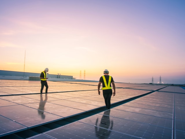 Two people standing on a roof with solar panels.